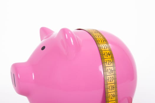 Measure tape and pink piggy bank, isolated on white background.