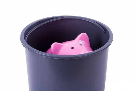 Pink piggy bank stacked in black bucket, isolated on white background.