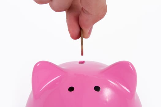 Coin holding by a human hand, fingers and pink piggy bank, isolated on white background.