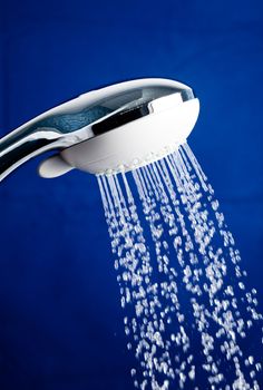 Shower head with running water against blue background