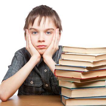 Portrait of upset schoolboy sitting at desk with books holding his head