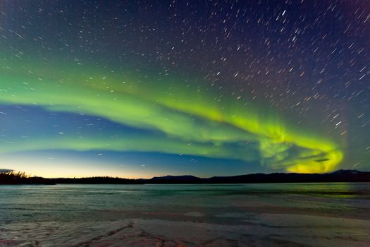 Intense Northern Lights or Aurora borealis or polar lights and morning dawn on night sky over icy landscape of frozen Lake Laberge Yukon Territory Canada