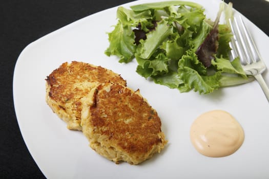 Fresh crab cakes on a white plate with sauce and a salad of field greens