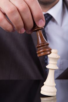 Businessman holding king and defeats opponent chess piece.