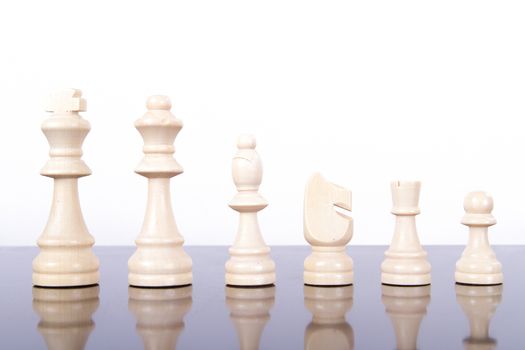 Full set of yellow wooden chess pieces on reflective glass table, isolated on white background.