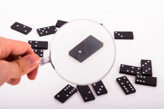 Business concept, hand holding magnifying glass and searching, black domino standing out from the crowd on white background.