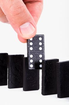 Hand holding black domino and building a line from dominoes, isolated on white background.