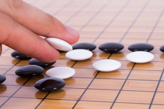 Close up view of hand playing black and white stone pieces on Chinese go game board.