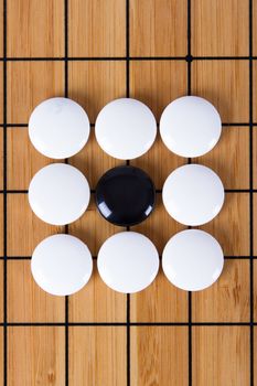 Black stone standing out from white pieces on Chinese go game board.