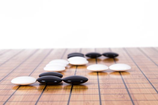 White stone standing out from black pieces on Chinese go game board, isolated on white background.