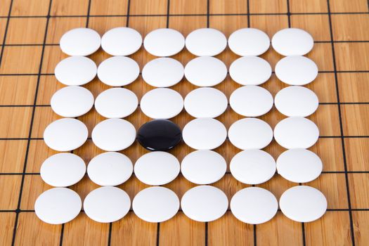 Black stone standing out from white pieces on Chinese go game board.