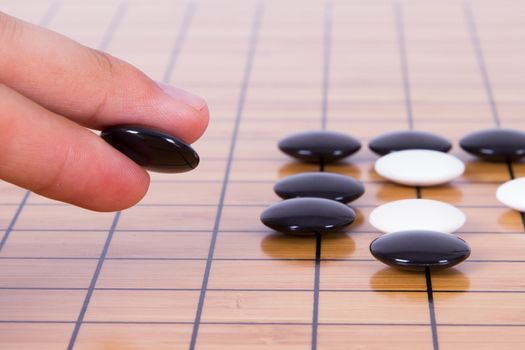 Close up view of hand playing black and white stone pieces on Chinese go game board.