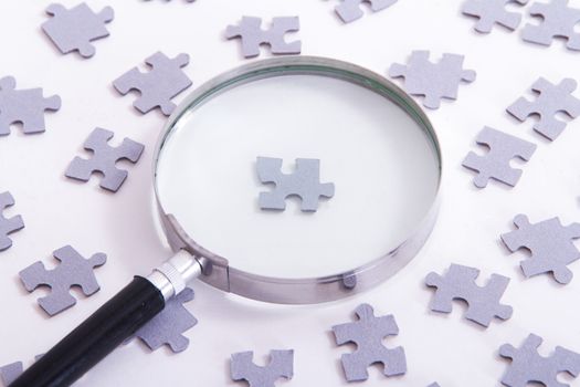 Hand holding classic style magnifying glass and searching leader puzzle piece among others on white.