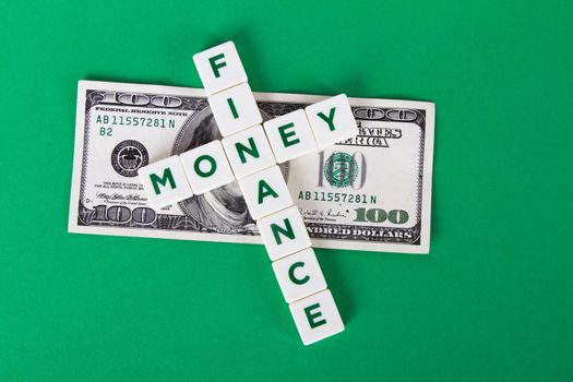 Finance and money words in letters with one hundred dollar bill on green background.