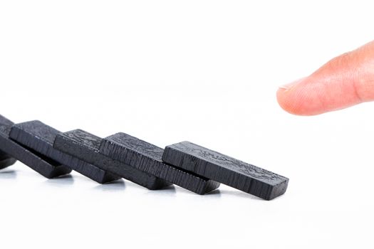 Fallen black dominoes and index finger, isolated on white background.