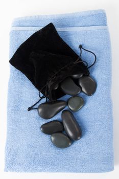 Black massage stones with soft case and blue towel, top view, isolated on white background.