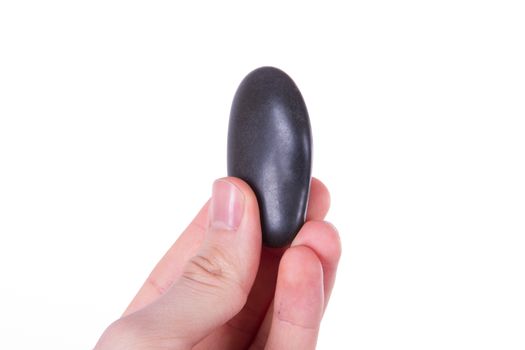 Hand holding and showing single black massage stone, isolated on white background.