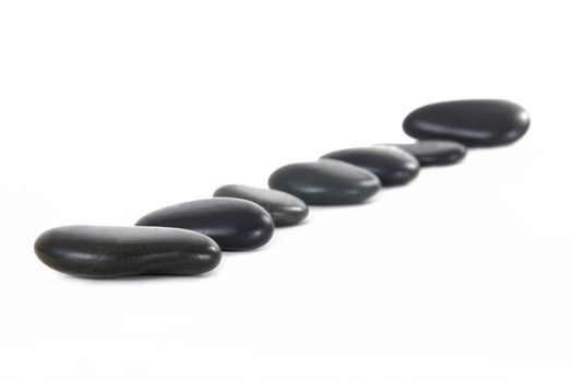 Black massage stones in a row, isolated on white background.