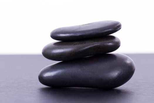 Three black massage stones balanced on black table, isolated on white background.