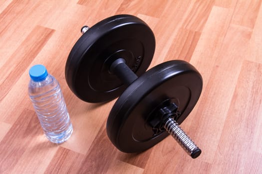Black dumbbell and plastic water bottle on studio.