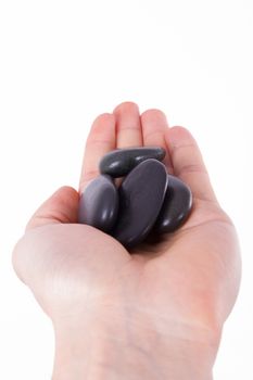 Hand holding and showing black massage stones, isolated on white background.