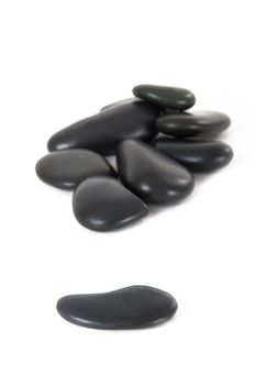 Single black massage stone standing out from the crowd, isolated on white background.