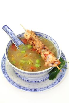 a bowl of chicken consomme and a chicken skewer