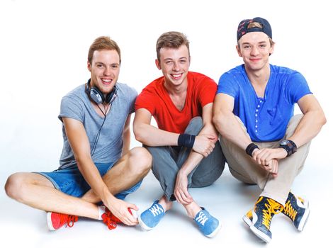 Three young happy smiling teenagers sitting on the floor. Isolated on white background.