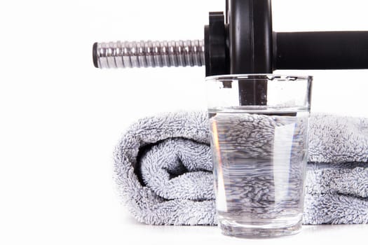 Close up of black gym barbell, dumbbell with disks, glass of clean water and blue towel, isolated on white background.