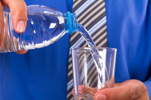 Water pouring into glass from plastic bottle by businessman.