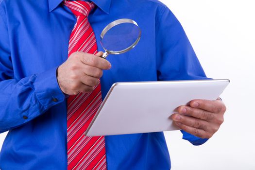 Businessman with red tie and blue shirt holding magnifying glass to tablet, isolated on white background.