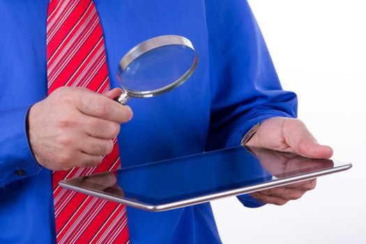 Businessman with red tie and blue shirt holding magnifying glass to screen of tablet, isolated on white background.