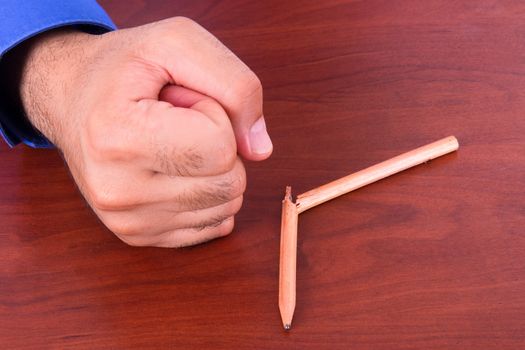 Angry businessman hand as punch and broken pencil on wooden table.
