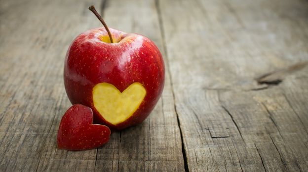 A red apple with engraved heart on wood background