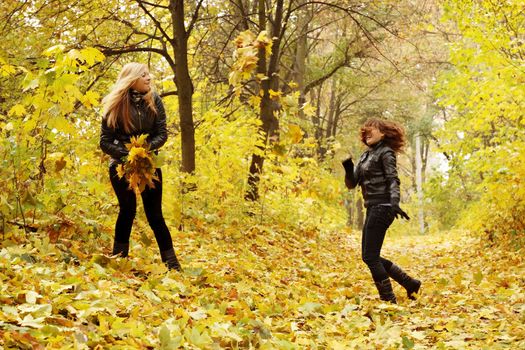 two friends throw each other autumn leaves