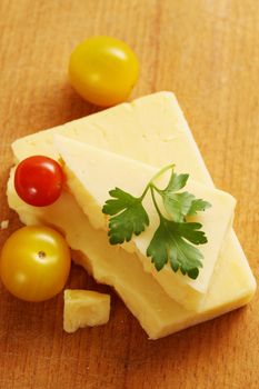 piece of cheese with small tomatoes on a wooden board