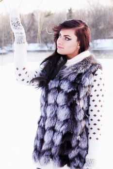 Young beautiful girl in a fur vest catches snow