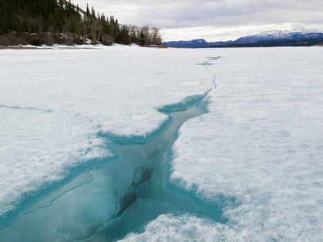 Open water in crack of ice sheet cover of wintery frozen Lake Laberge Yukon Territory Canada