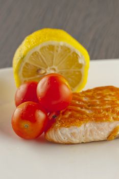 Piece of salmon over a white plate, with tomatoes and lemon