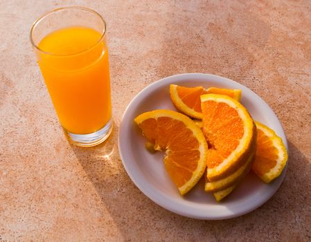 Sliced orange on a white plate and a glass of orange juice.