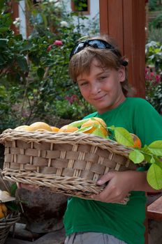 A boy carries a basket of oranges.