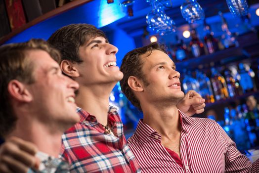 Three men stand in a row embracing smile and look in front of you, sports fans