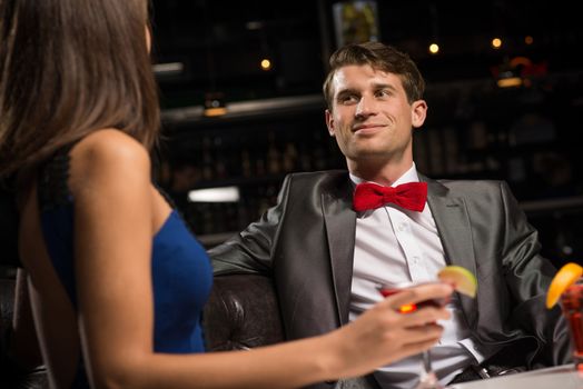 portrait of a man in a nightclub, sitting on the couch and talking with woman