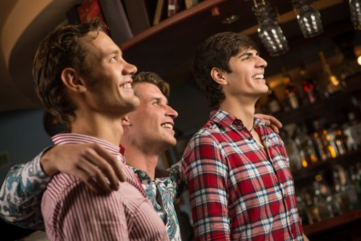 Three men stand in a row embracing smile and look in front of you, sports fans