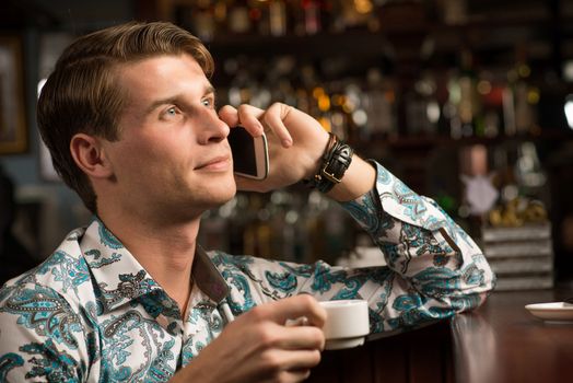 young man at the bar on the phone and drinking coffee