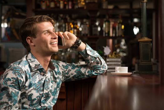 young man at the bar on the phone and drinking coffee