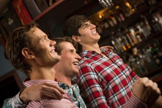 Three men stand in a row embracing smile and look in front of you, sports fans