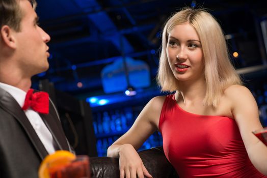 portrait of a woman in a nightclub, sitting on the couch and talking with man