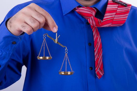 Businessman with red tie and blue shirt holding golden scales unbalanced, isolated on white background.