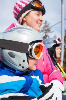 Portrait of happy boy in ski goggles and a helmet with his mother and sister on the ski lift